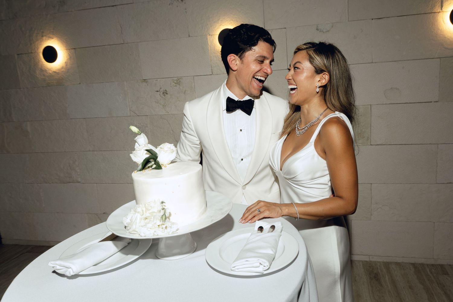 Wedding couple laughing while playfully feeding each other cake at their reception.