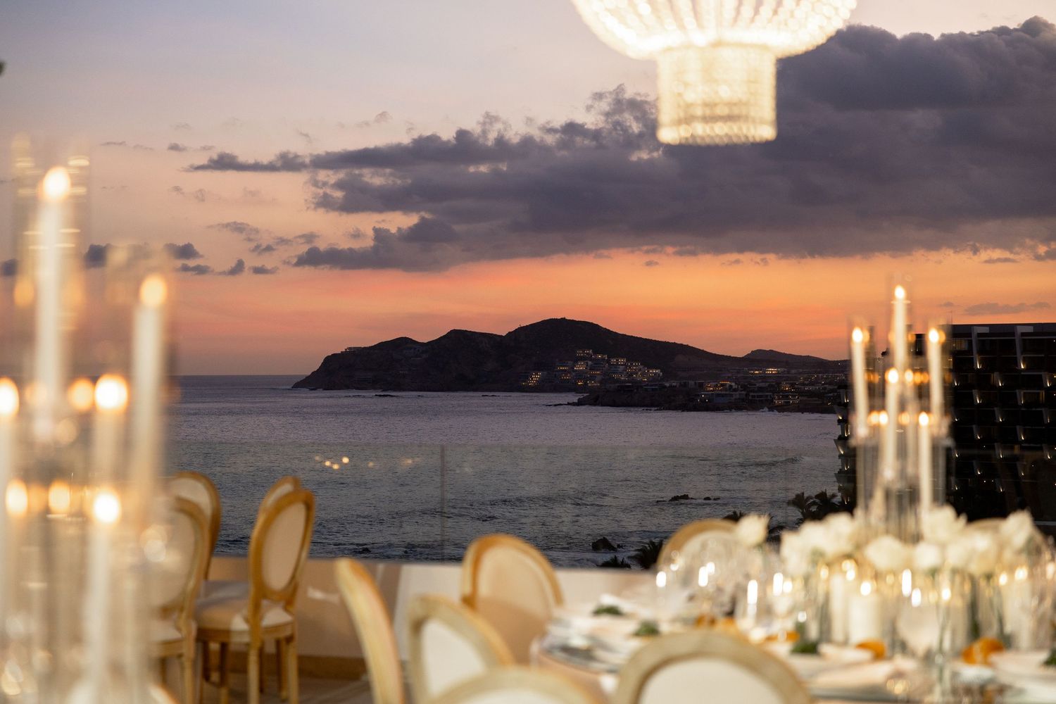 Romantic coastal wedding reception tables set against a dramatic sunset backdrop.