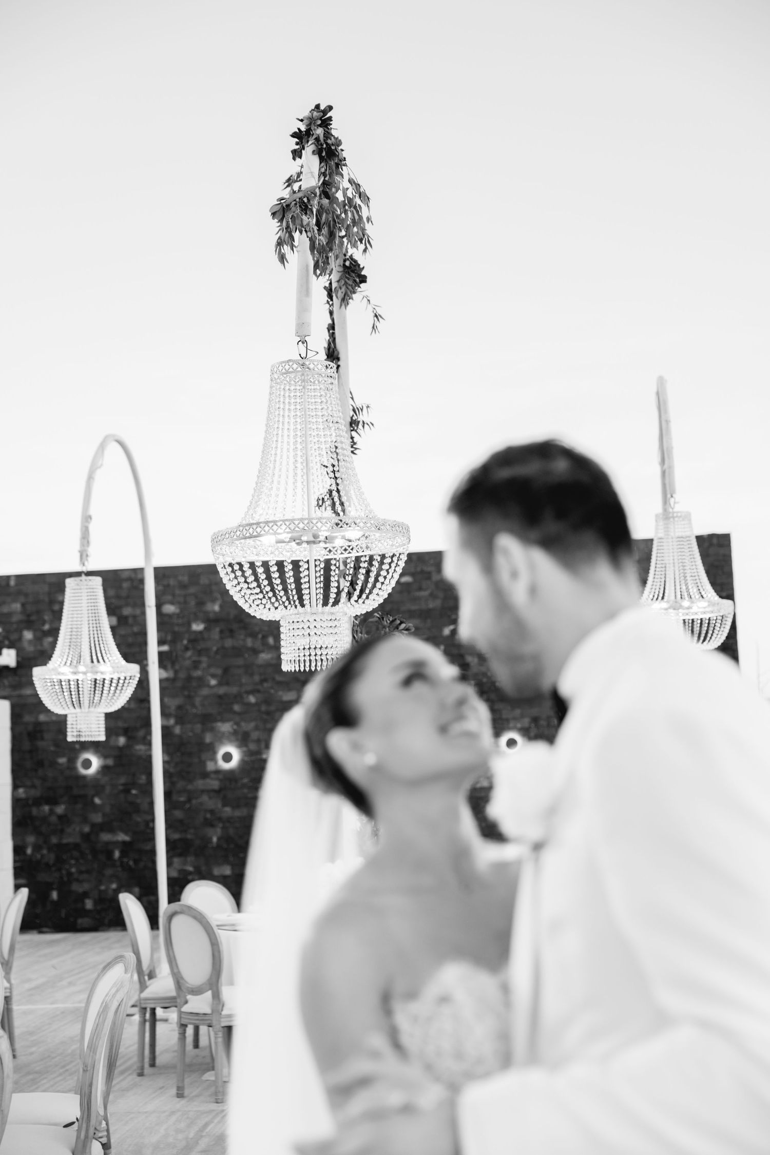Romantic wedding moment under crystal chandeliers and hanging greenery at sunset.