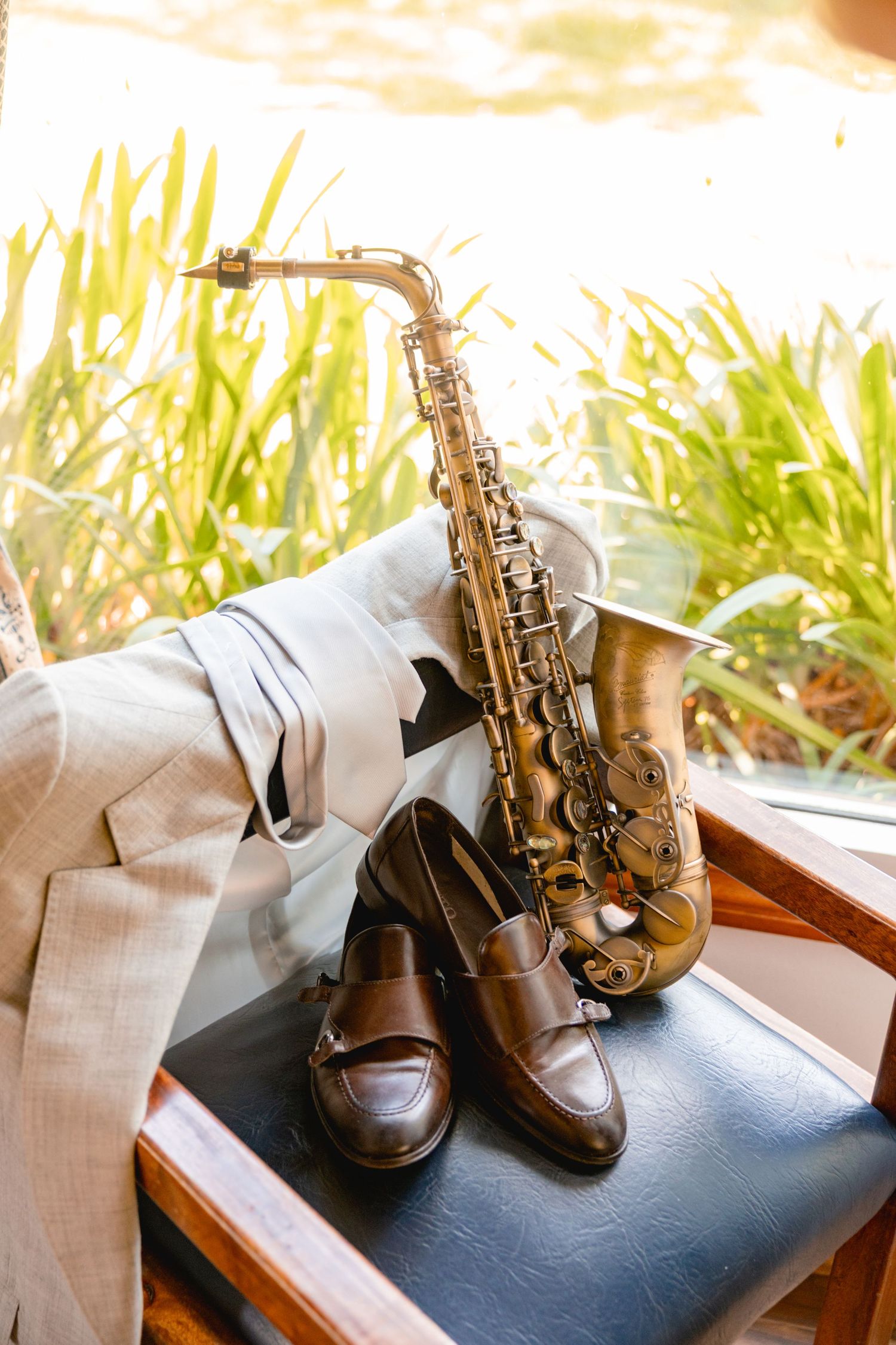 Vintage saxophone and brown leather shoes arranged on chair in natural sunlight.