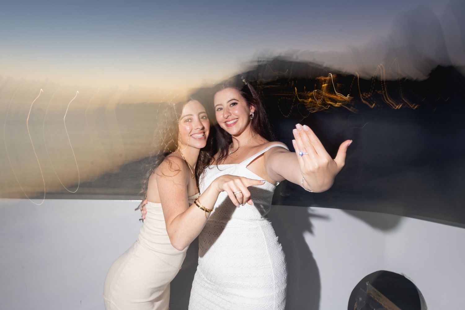 Two people in white dresses dance together on a beach at sunset, creating a romantic silhouette against the sky.