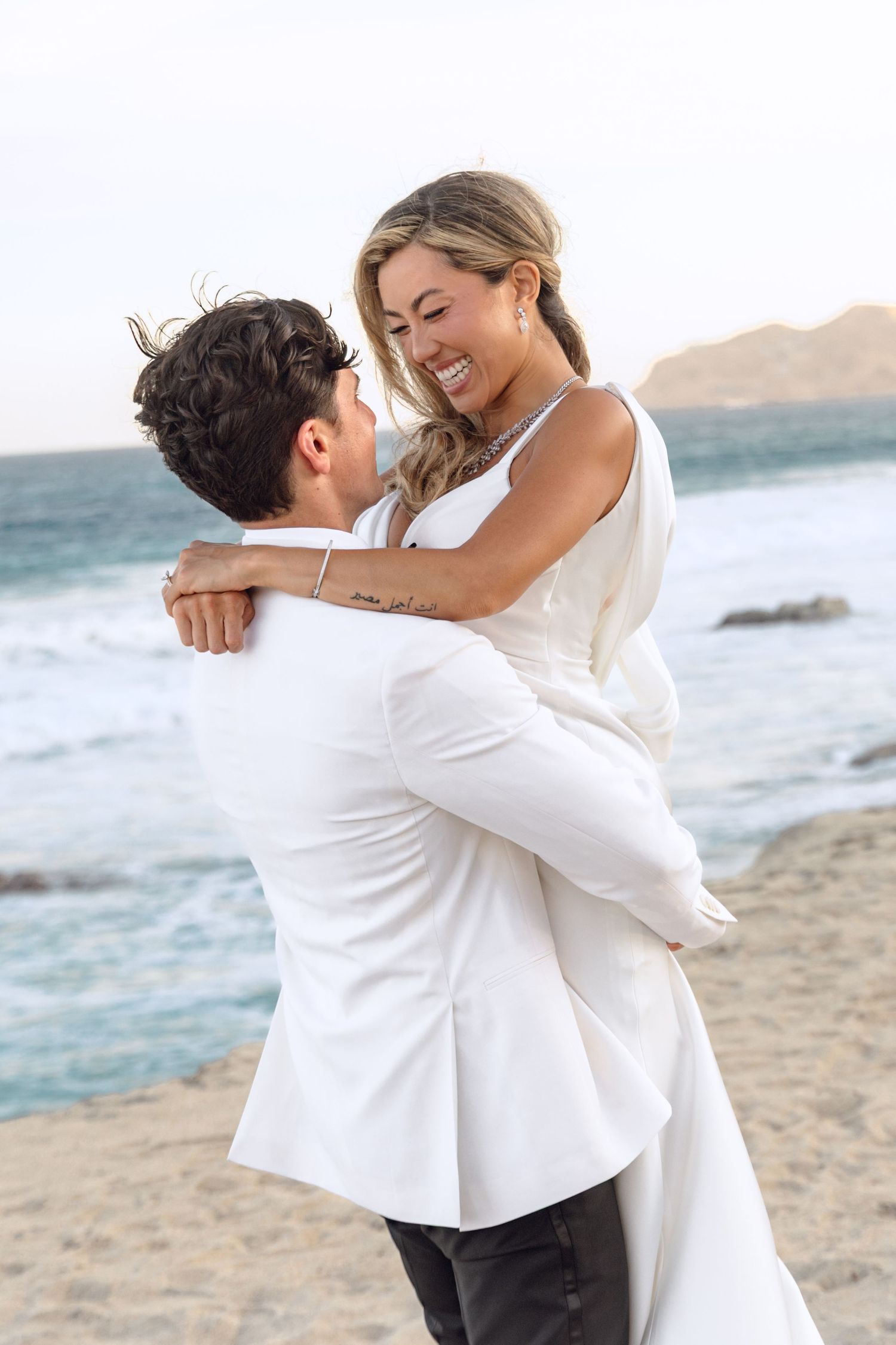 Joyful wedding moment with couple embracing and laughing on beach.