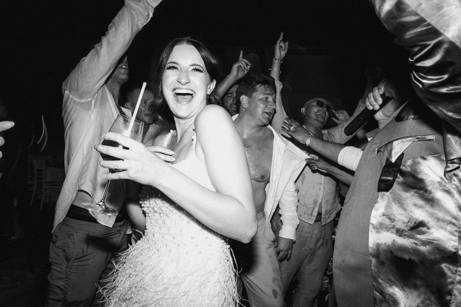 Dancing guests celebrate on a dark dance floor with festive lighting at a wedding reception.