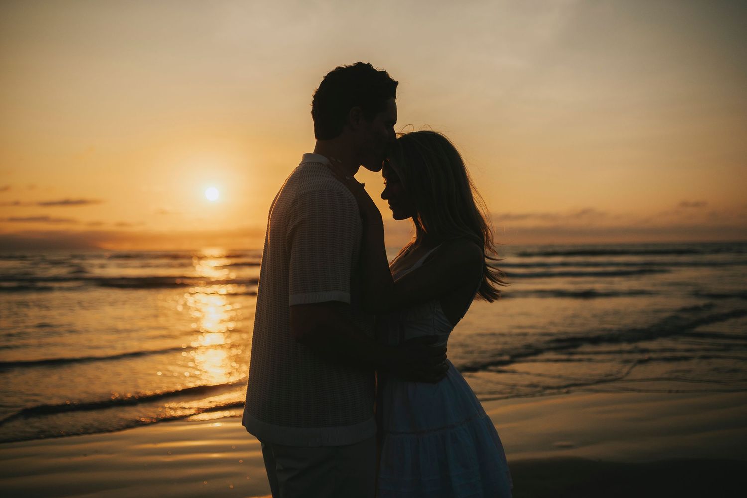 Silhouettes of people embracing against dramatic ocean sunset backdrop.