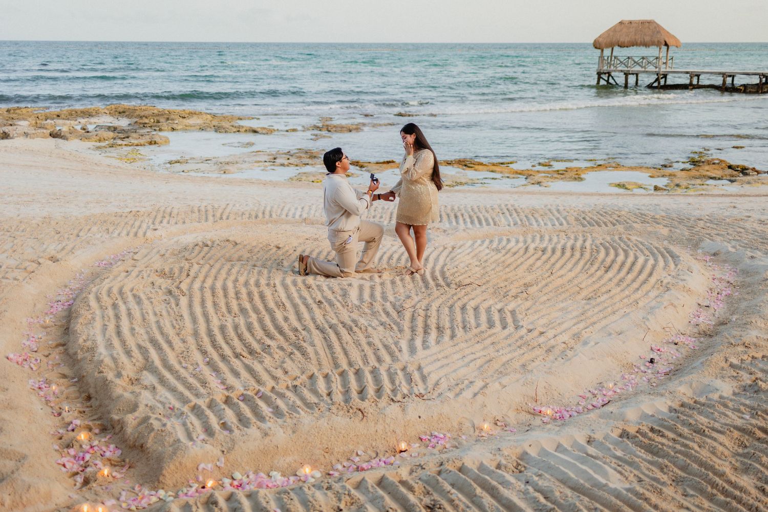 A heart shape drawn in the sand on a tropical beach with ocean waves in the background.