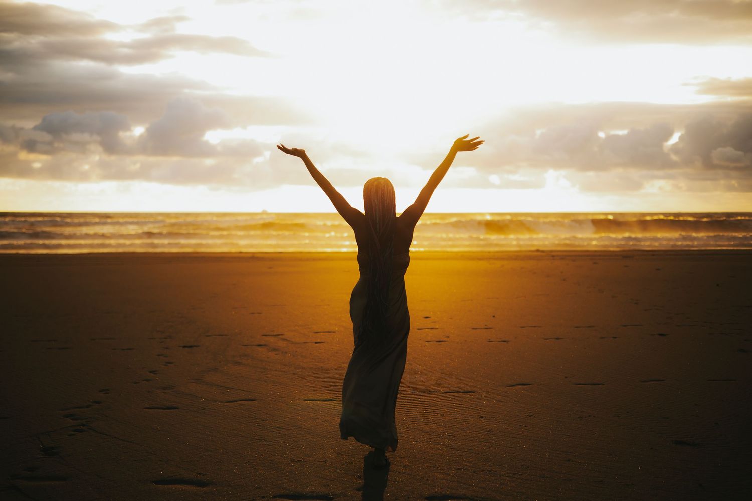 Silhouette of person with raised arms celebrating on beach at golden sunset.