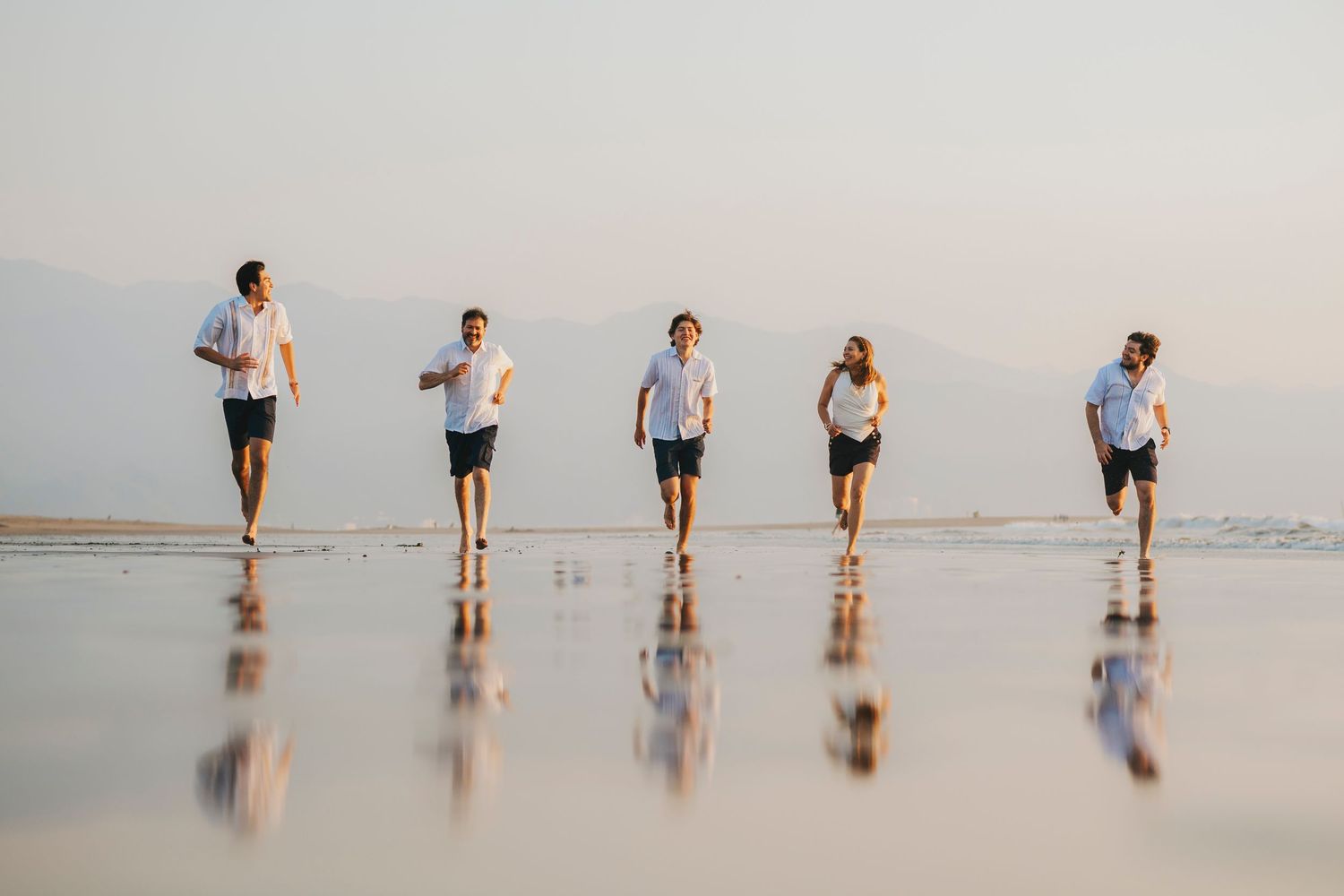 Group of friends jogging together on reflective wet beach sand at sunset.
