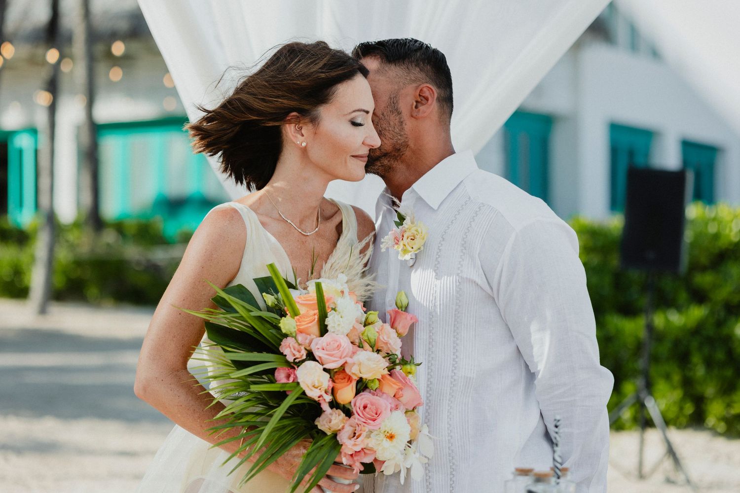 Couple sharing romantic moment against coastal backdrop with tropical flowers.