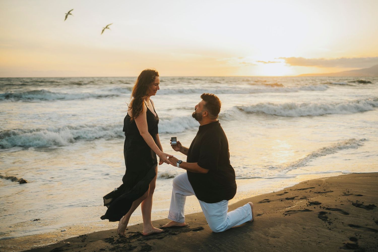 Romantic beach proposal scene at sunset with waves crashing in the background.