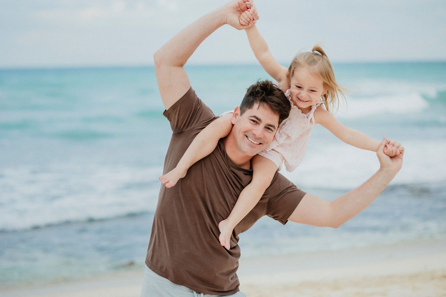 Playful beach photoshoot with people dancing and jumping in casual attire.