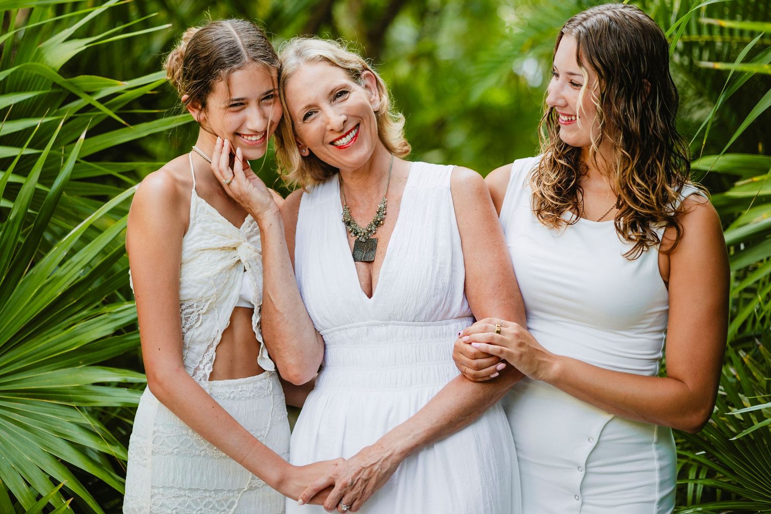 Family wearing white outfits poses among tropical palm leaves.