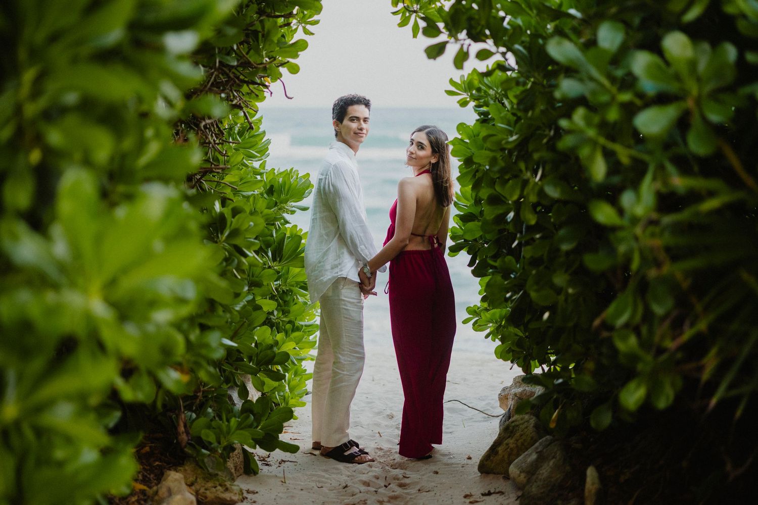 Intimate moment captured through lush green foliage at a tropical beach setting.