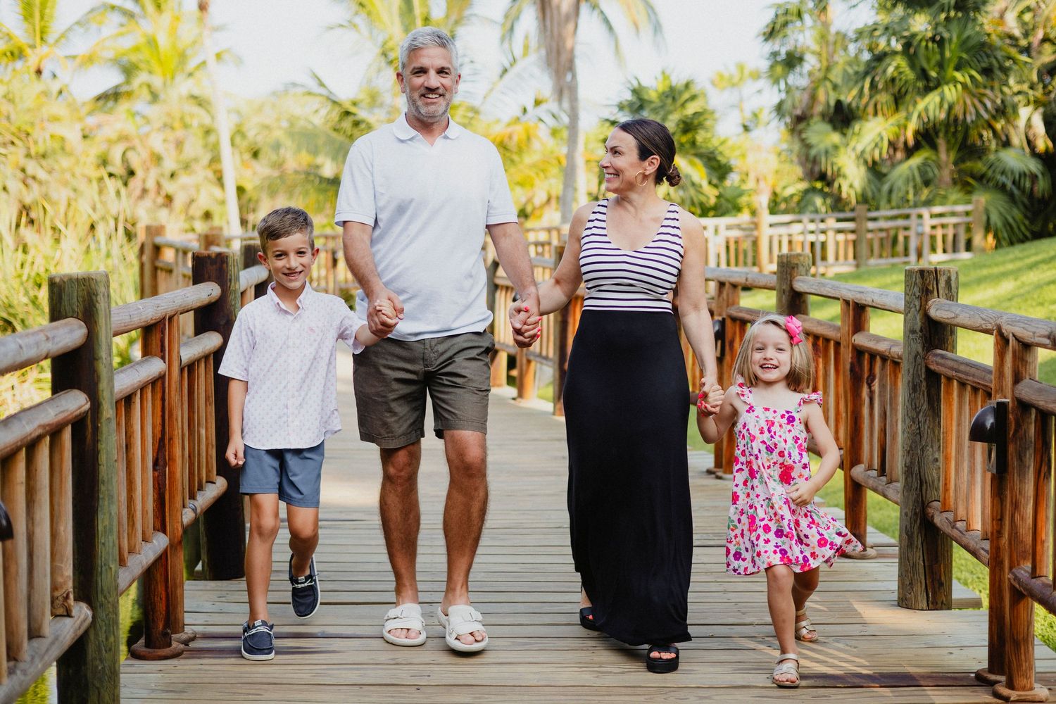 Family walking together on a wooden boardwalk surrounded by palm trees during sunset.
