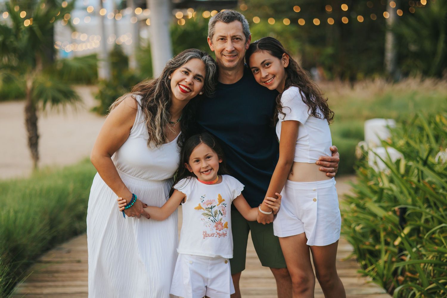 Family portrait session in a tropical garden setting with palm trees and string lights.