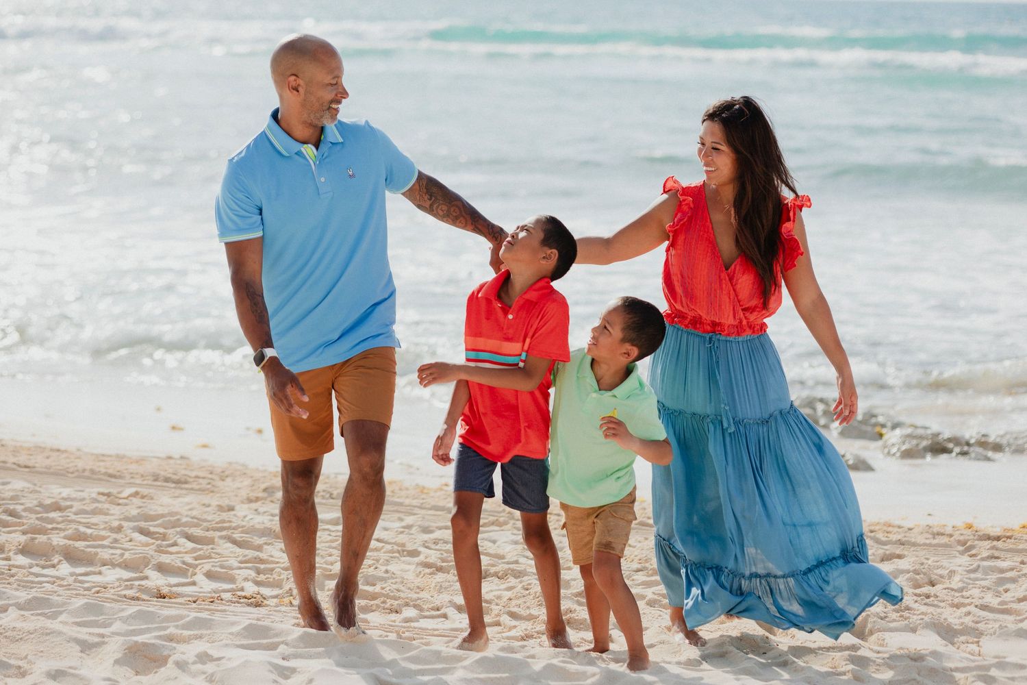 Family strolling along the beach in coordinated blue and coral outfits.