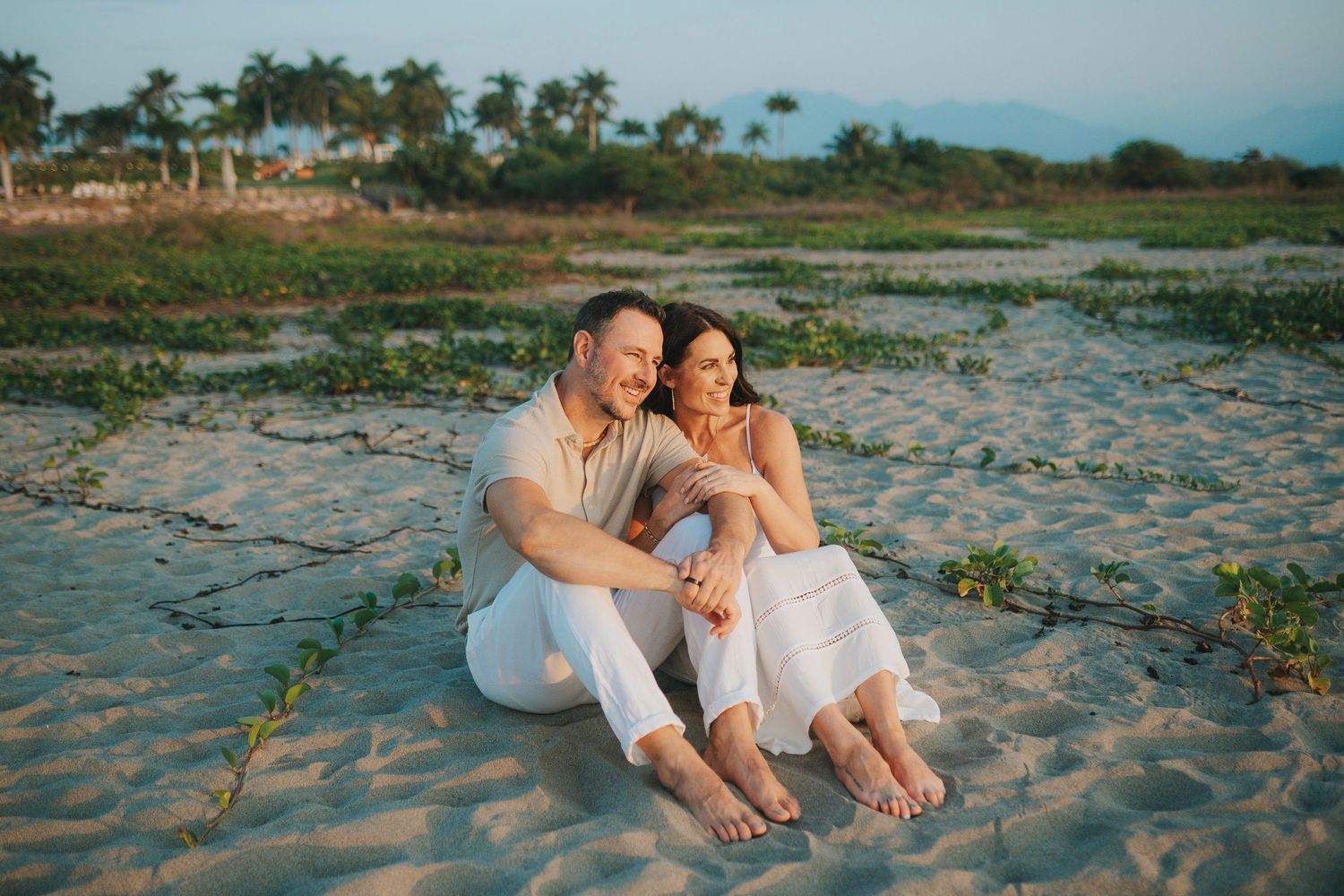 Couple sitting close together on a sandy beach during golden hour.