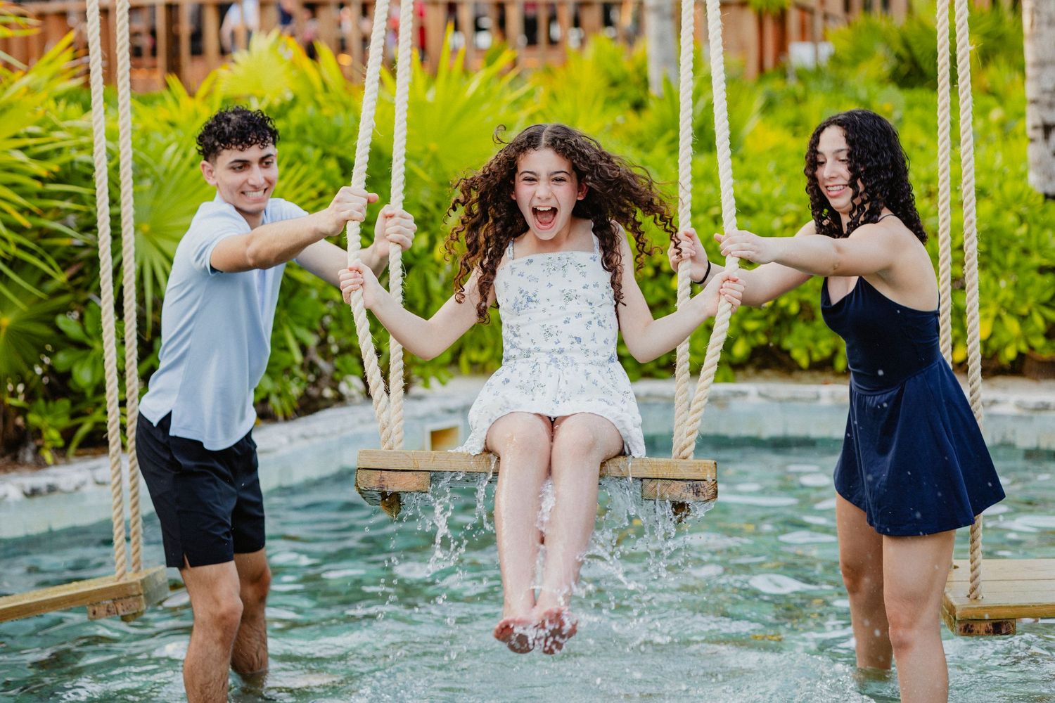 Friends having fun splashing water while swinging at outdoor pool area.