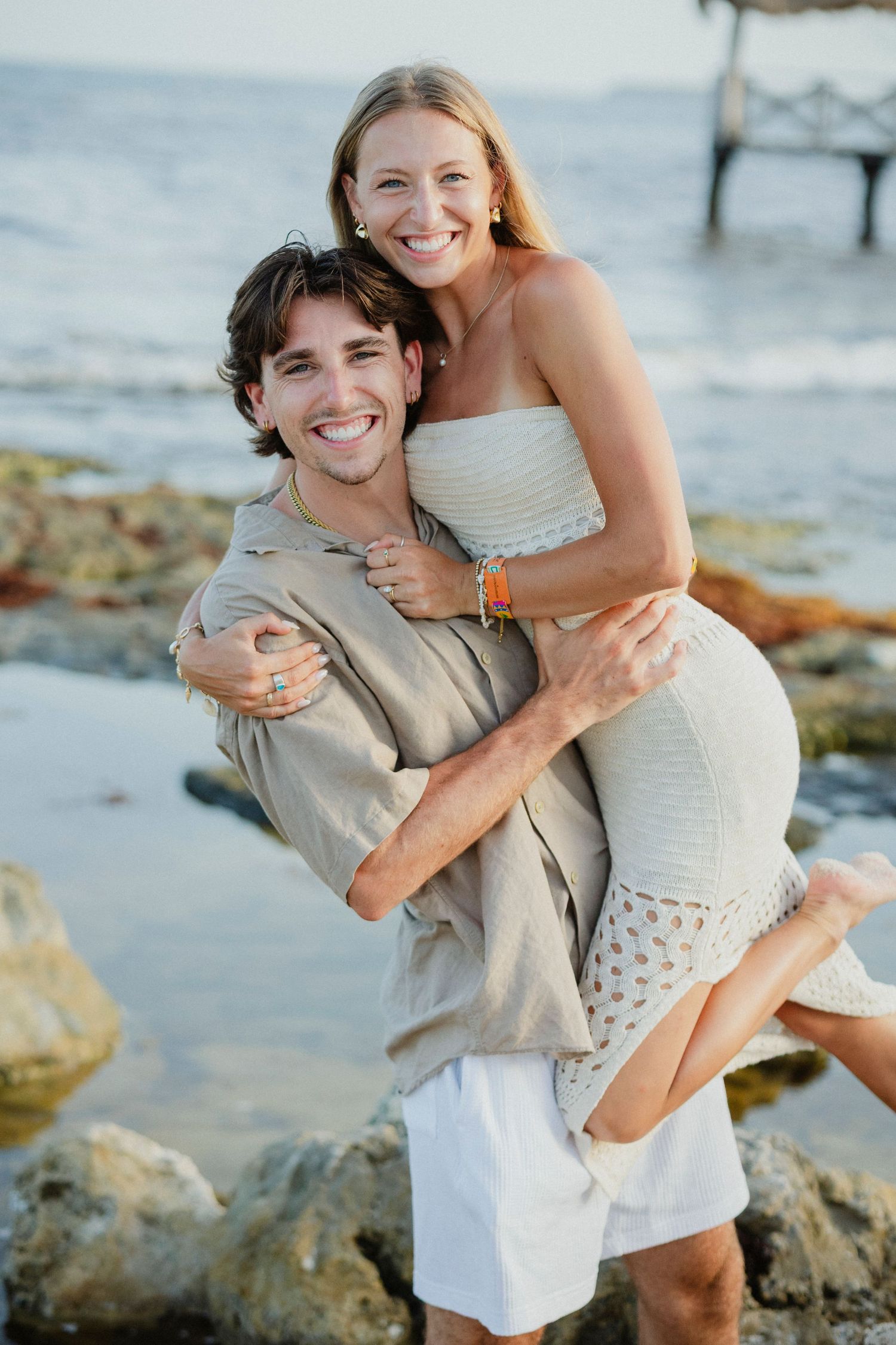 A couple embraces joyfully on a rocky beach during a romantic photoshoot.