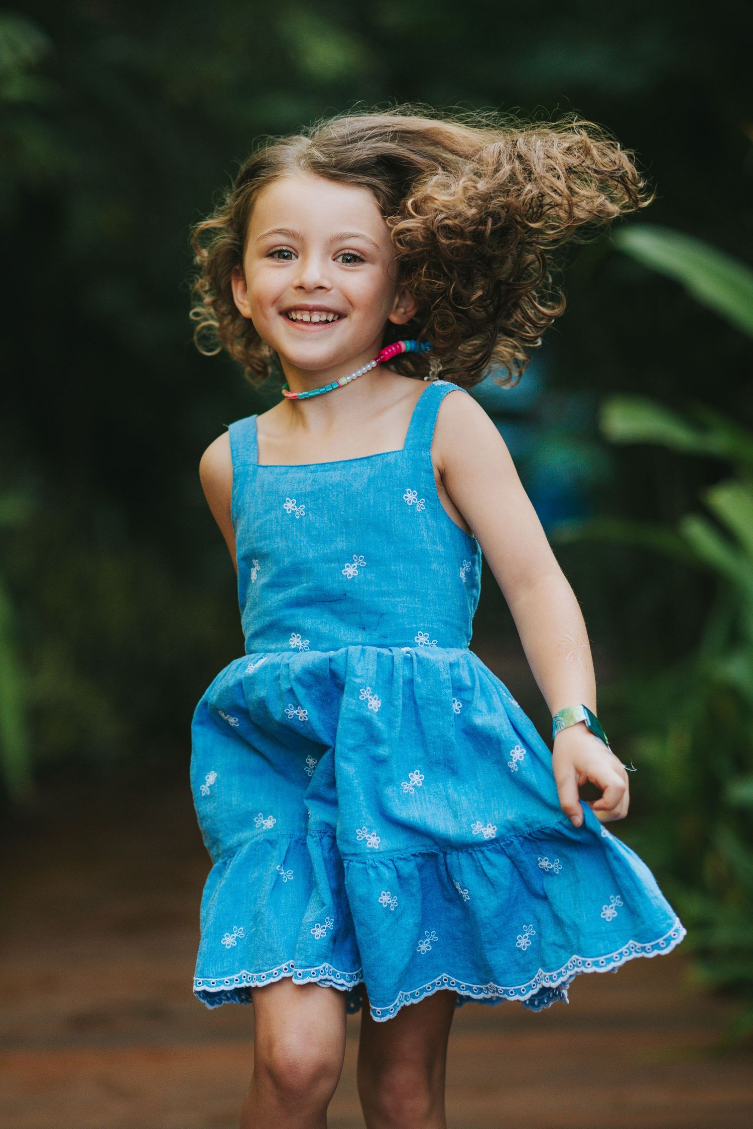 A child in a blue dress twirls and dances playfully outdoors.