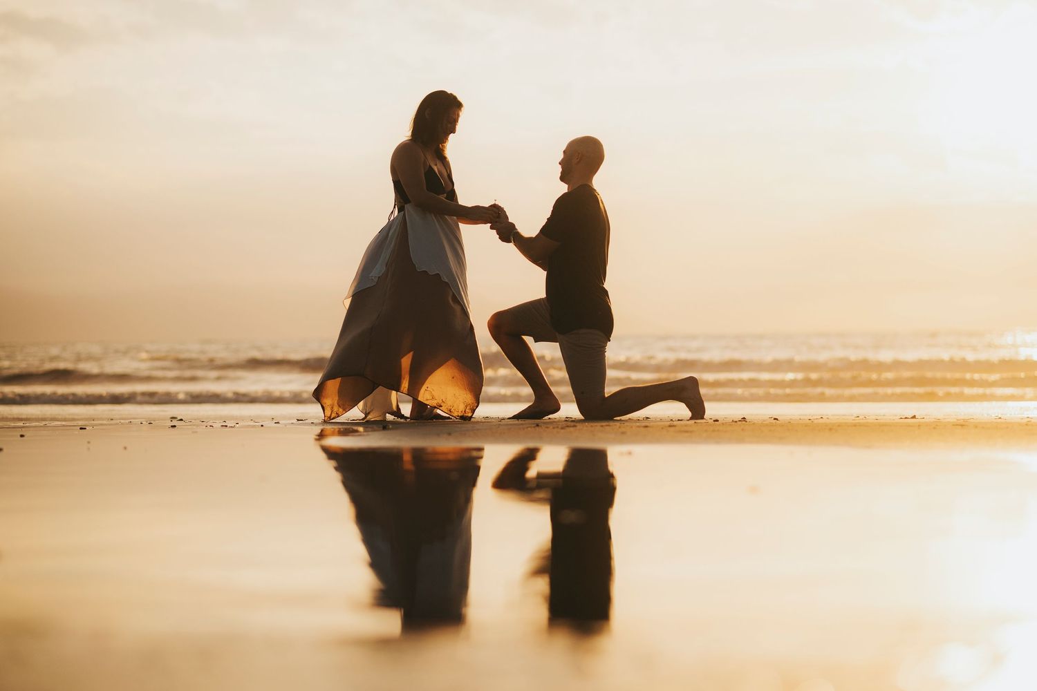 Romantic silhouettes against a golden sunset on a beach during a proposal moment.