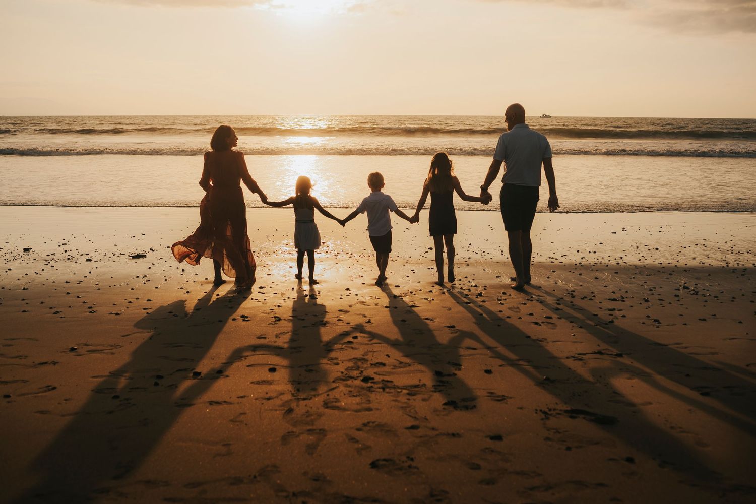 Silhouettes of a family walking along a beach at sunset casting long shadows.