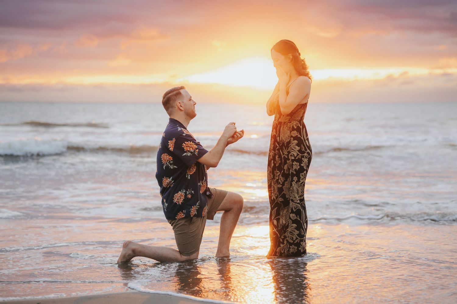 A romantic beach proposal silhouetted against a stunning sunset.