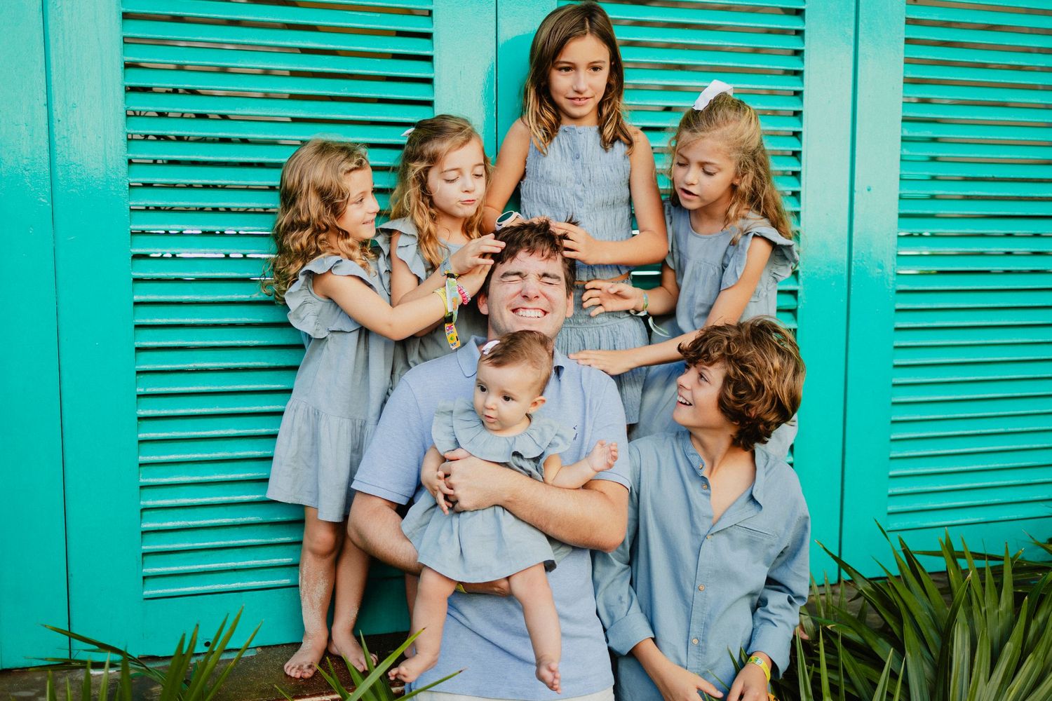 Group photo session against turquoise shuttered wall in coordinated blue outfits.