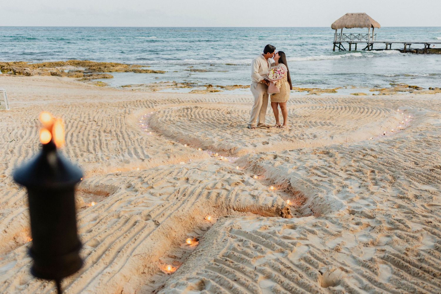 A heart pattern drawn in pristine beach sand with the ocean and pier visible in the distance.