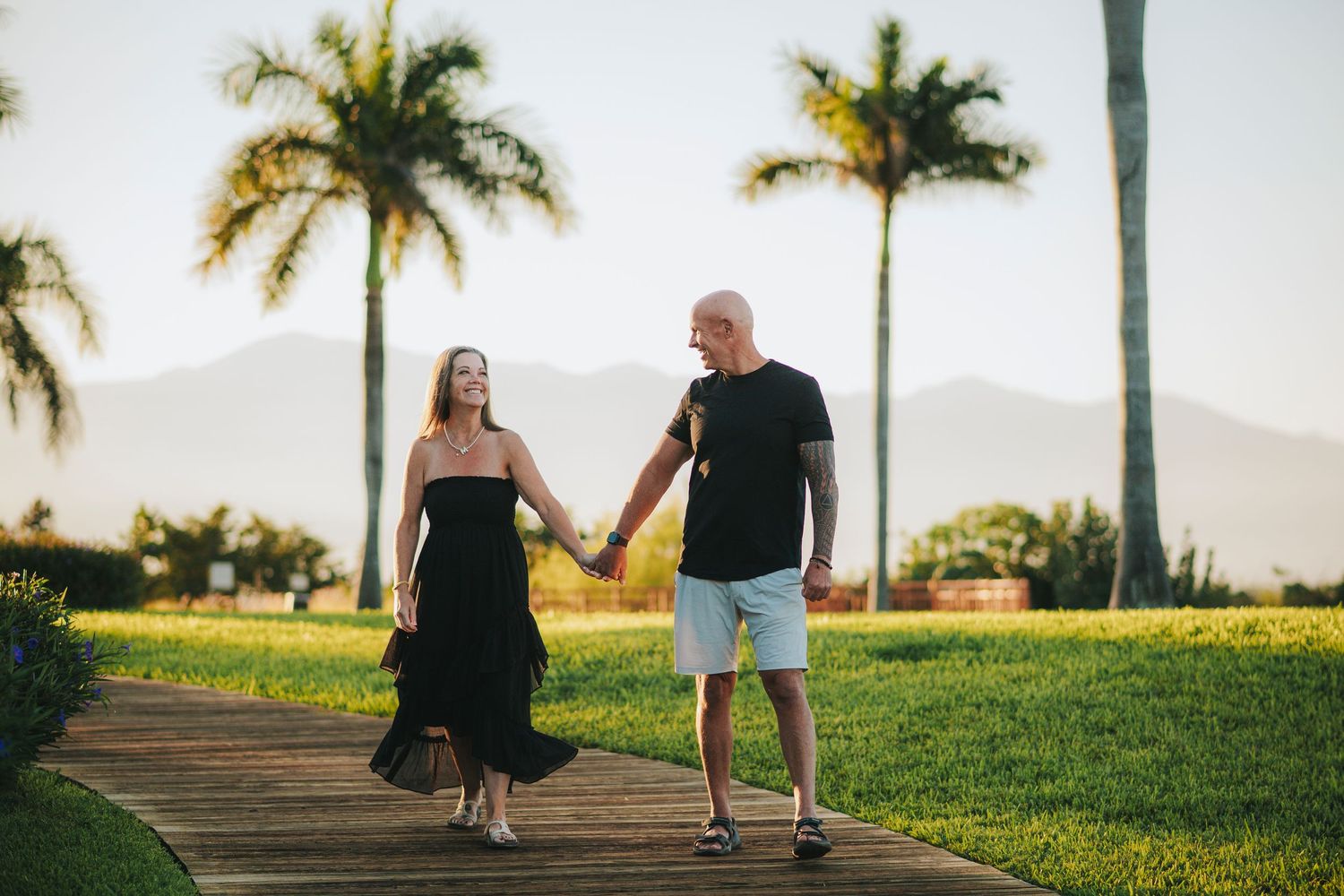 Couples walking hand in hand along a palm-lined path during golden hour.