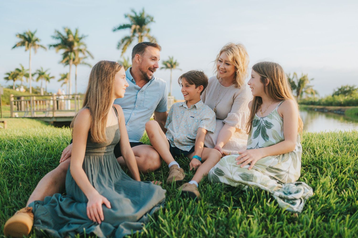 Family relaxing together on grass with palm trees in the background.