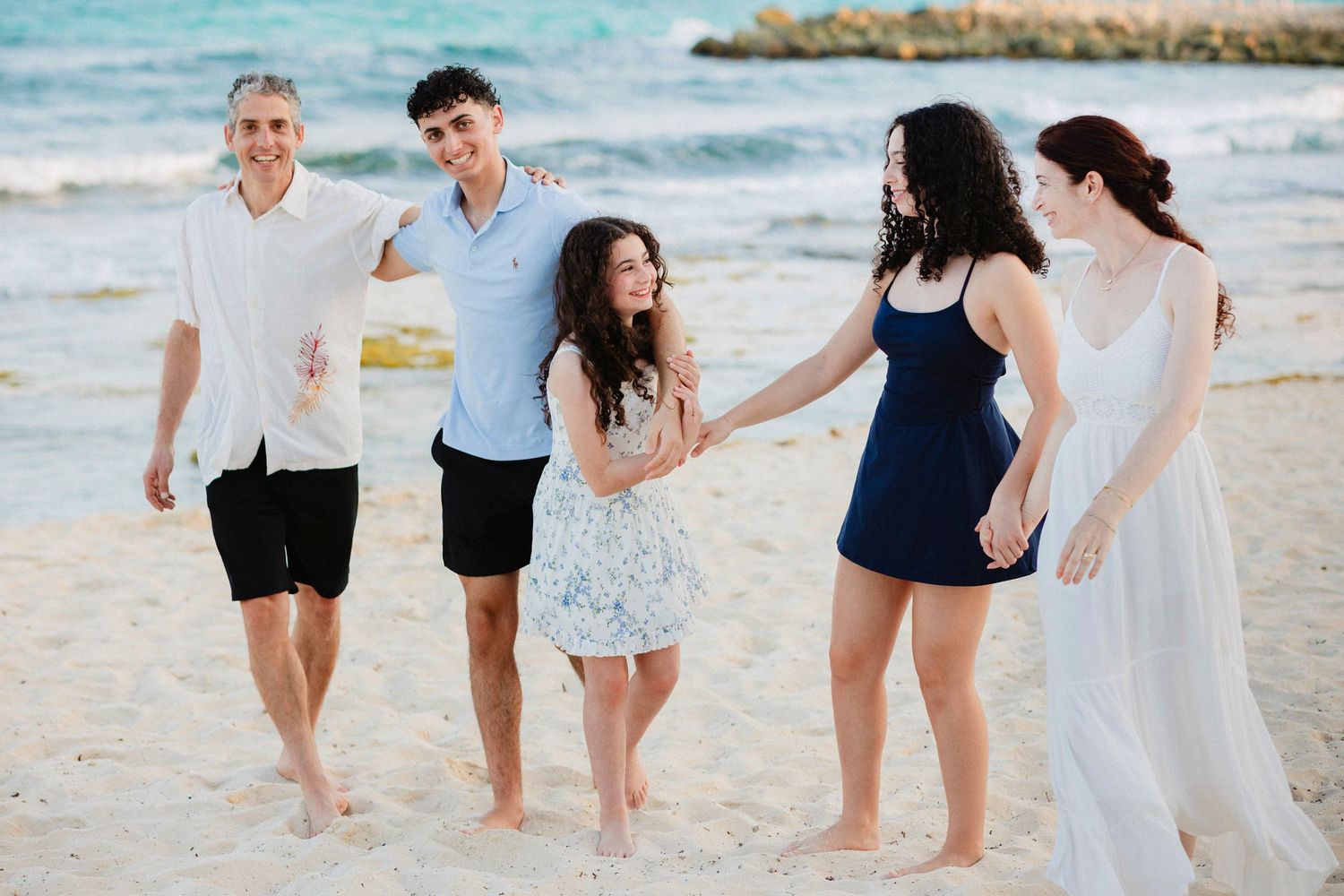 Family walking together along a scenic beach shoreline with turquoise waters and palm trees.