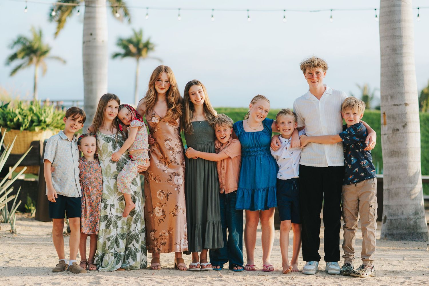 Extended family group photo with multiple generations posed together under palm trees.