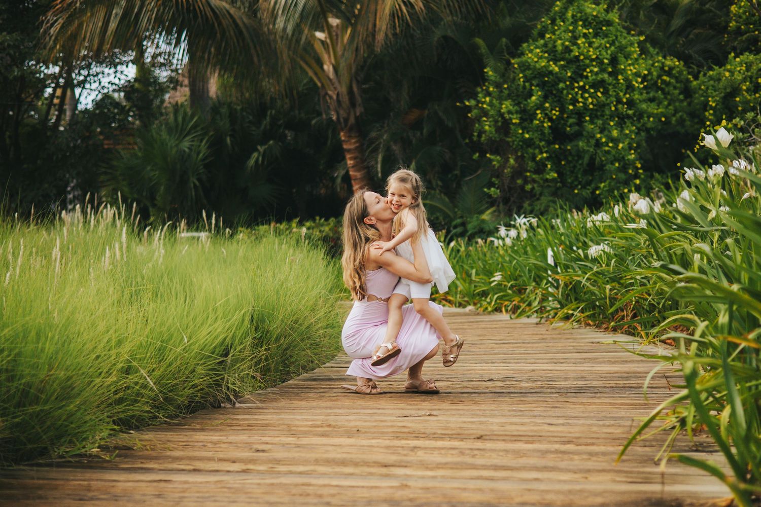 People having fun and posing on a wooden boardwalk surrounded by tropical plants.