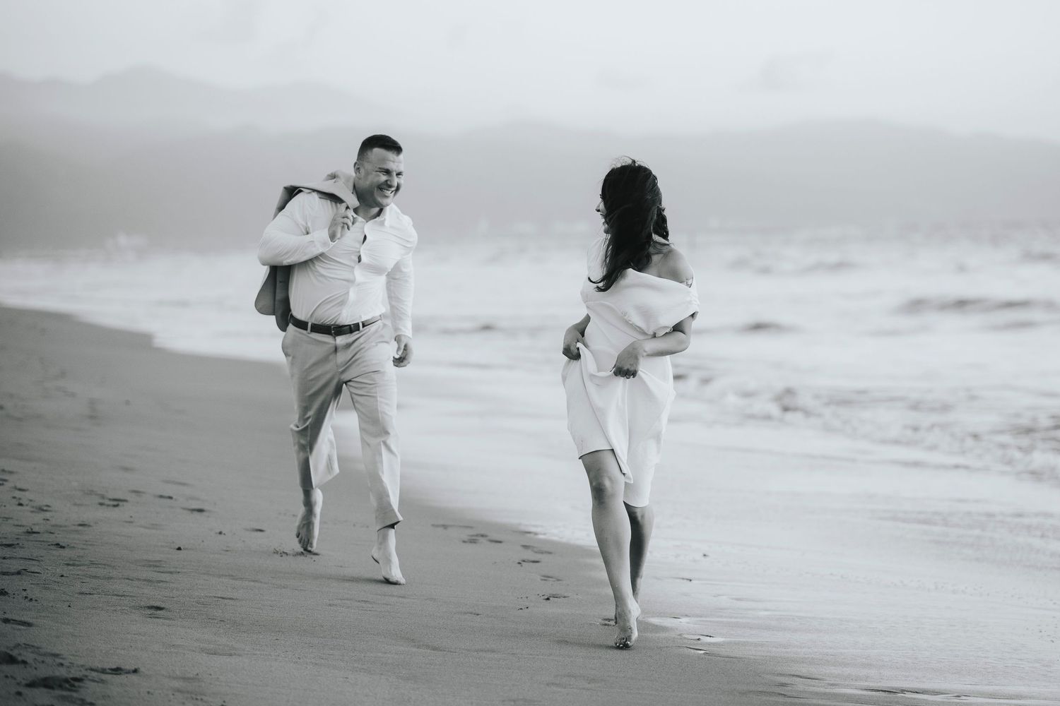 Family running and playing together along a misty beach shoreline in black and white.