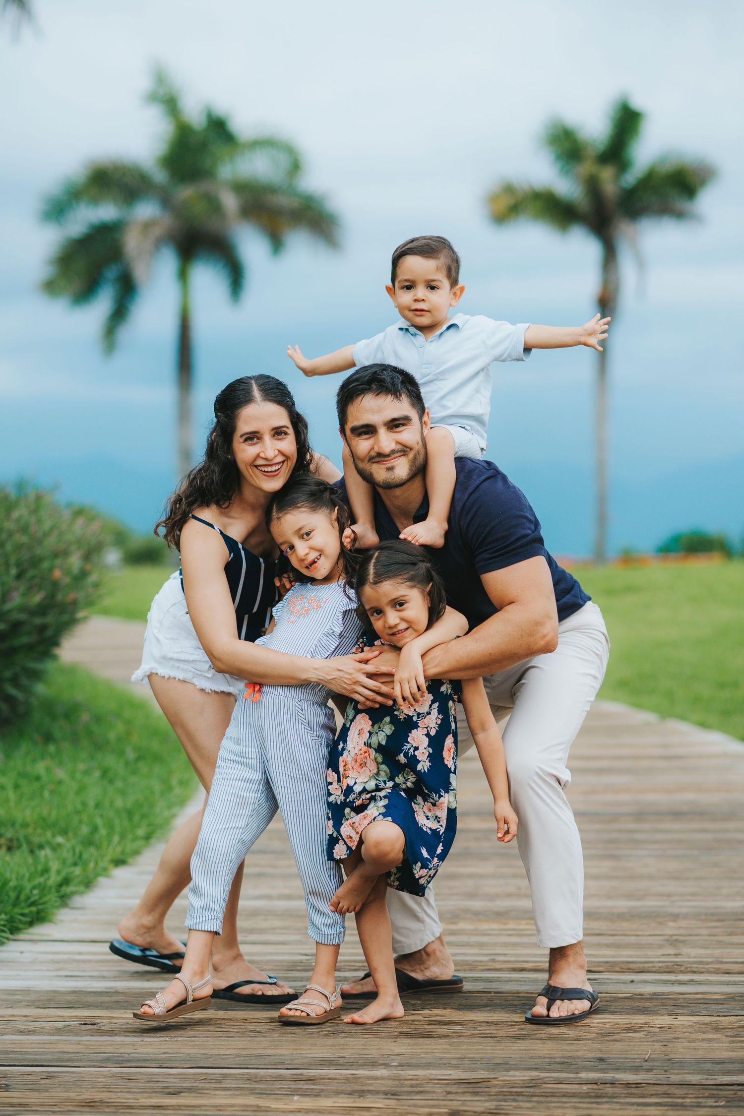 Happy family enjoying time together on a wooden walkway with palm trees and ocean views.
