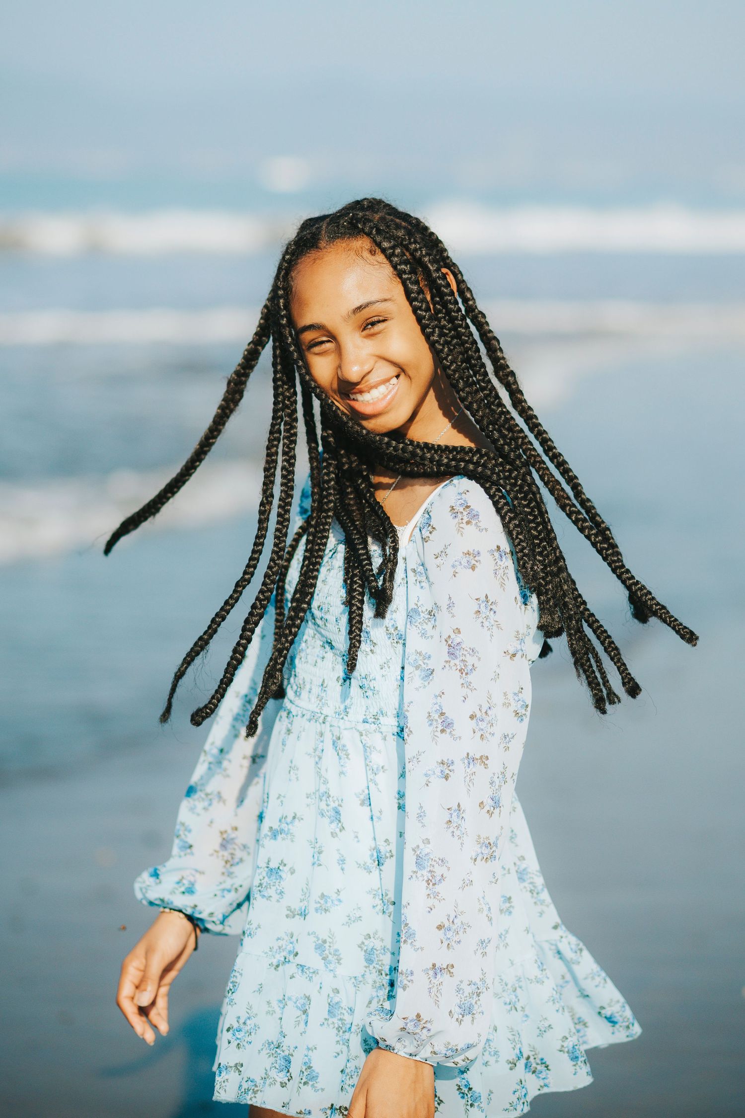 Young person in blue floral dress twirling and dancing on the beach at sunset.