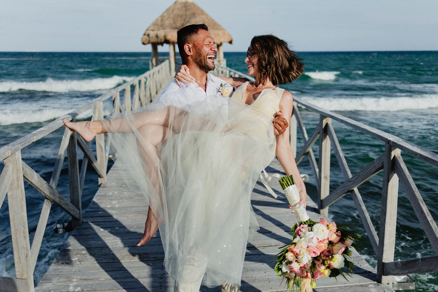 A romantic beach wedding ceremony setup with white decor and floral arrangements on a tropical shoreline.