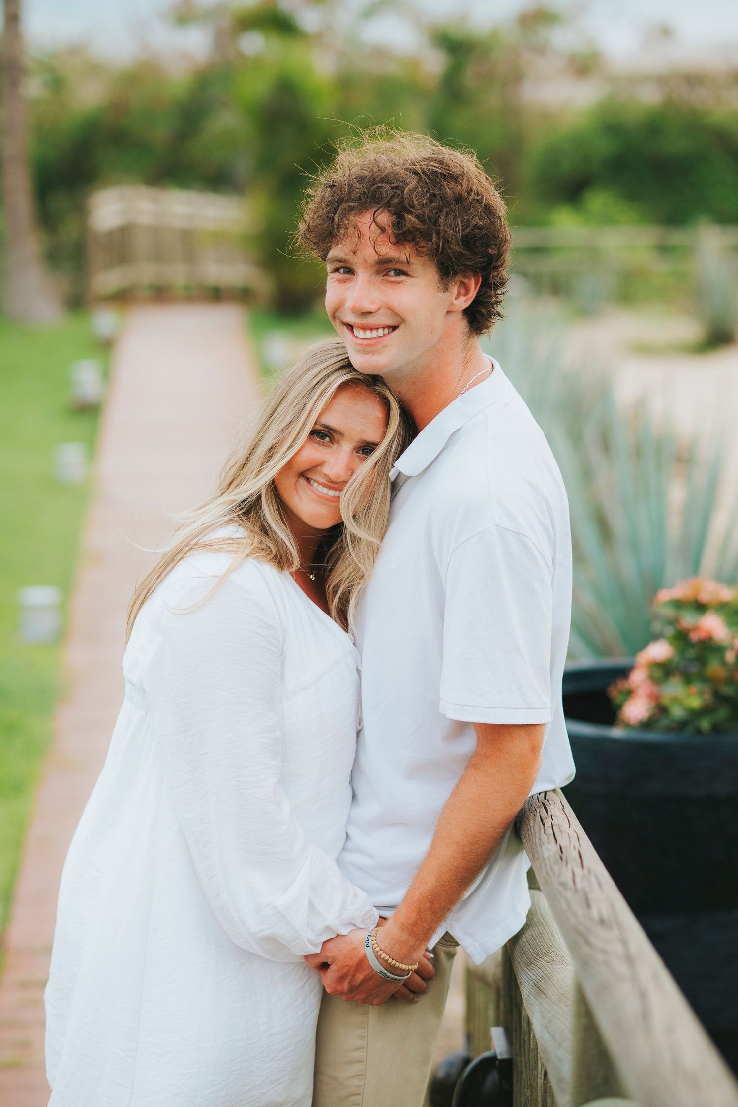 Couple in white outfits sharing intimate moments in a garden setting.
