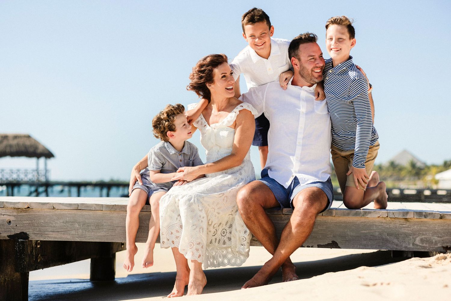 Family plays and laughs together on wooden boardwalk by the ocean.