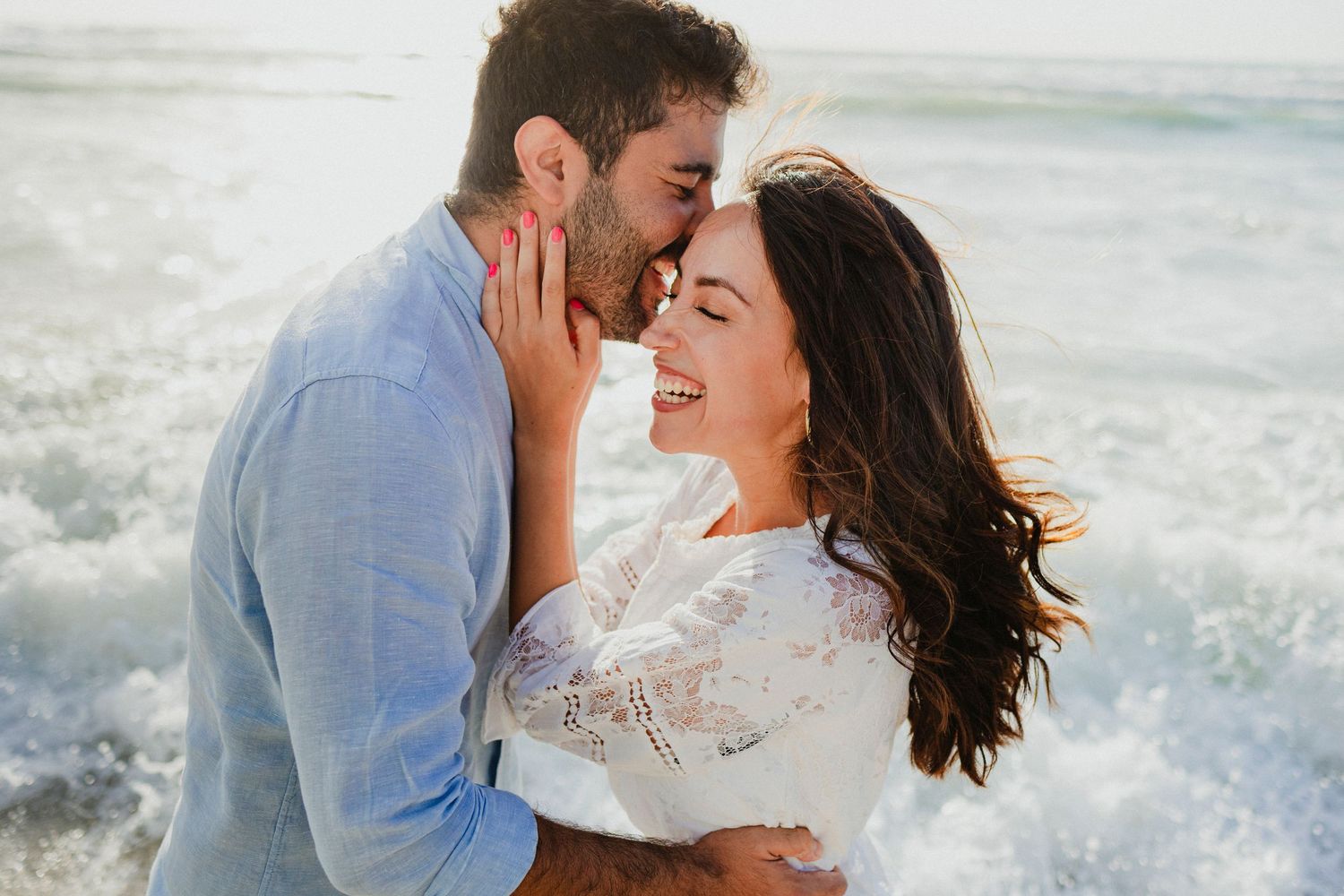 Couple embraces lovingly on a beach with ocean waves in the background.