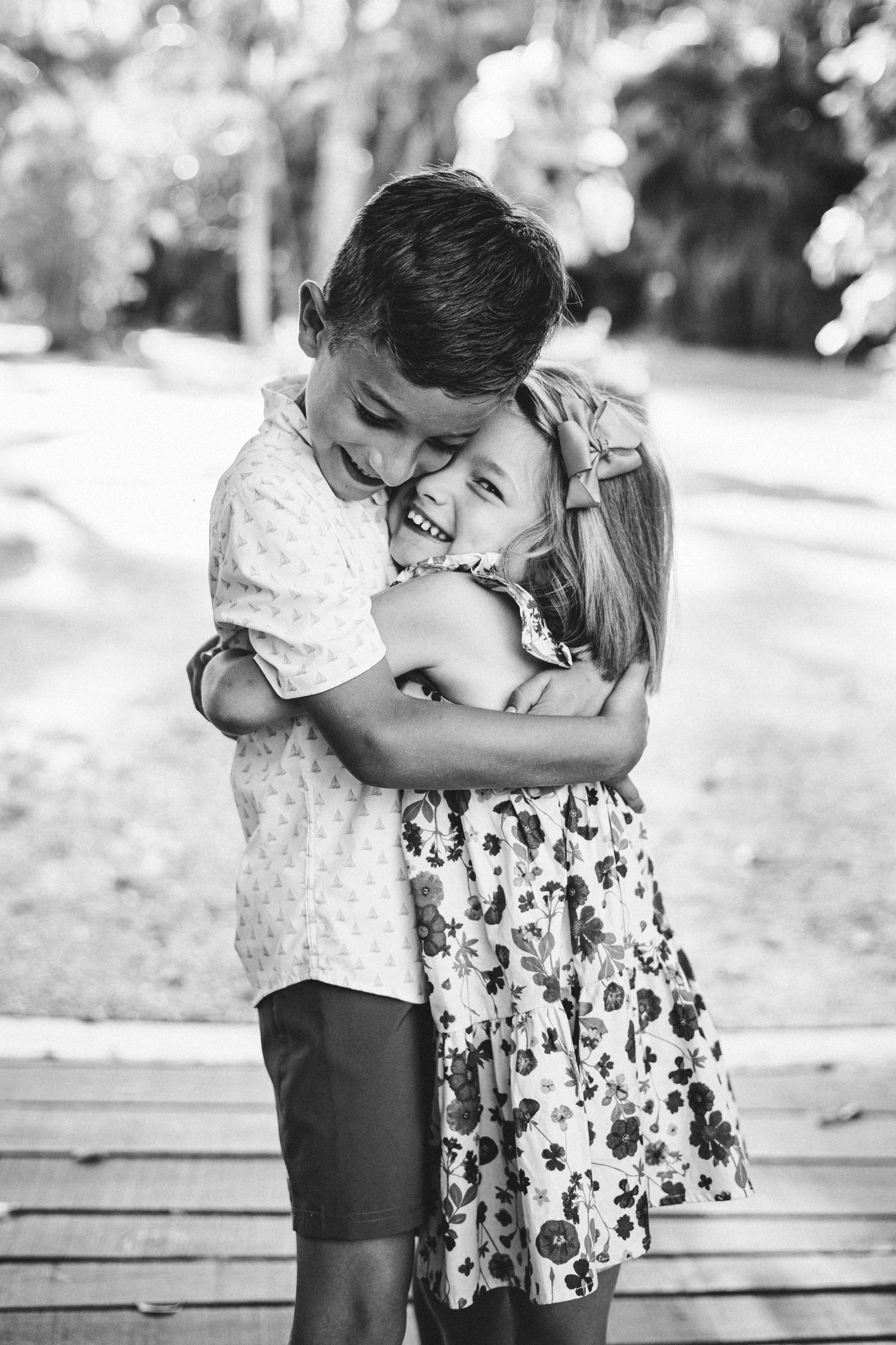 Black and white photo of two children sharing a sweet moment on a wooden bench.