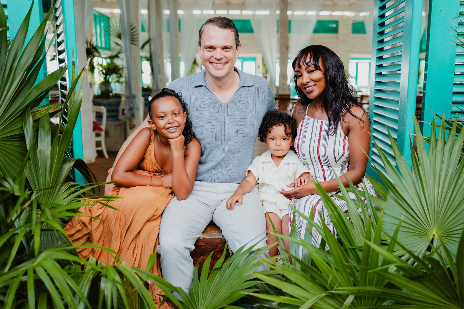 Family portrait session in a lush tropical garden setting with teal walls.