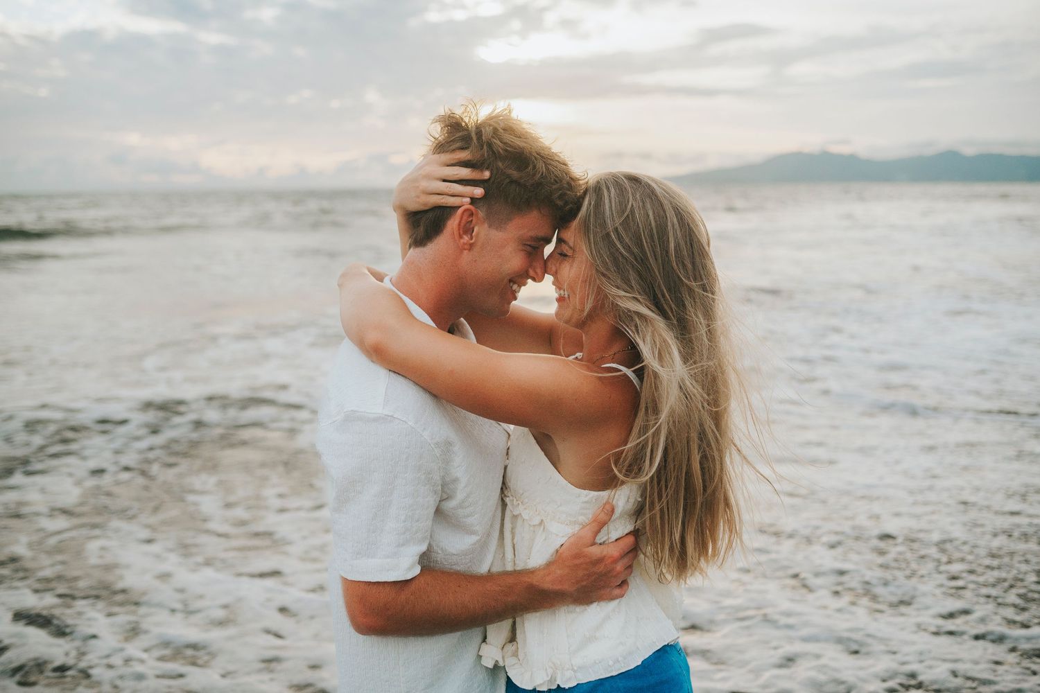 Romantic beach photoshoot with couple embracing during golden hour.