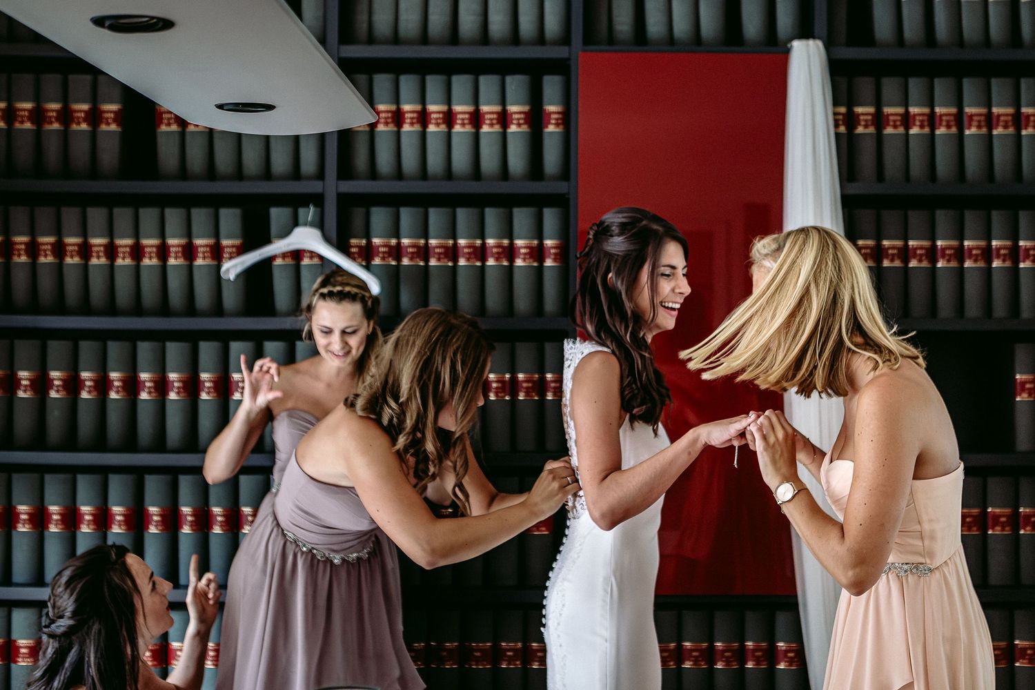 Wedding party members in pink and white dresses dance together in front of a law library bookshelf.