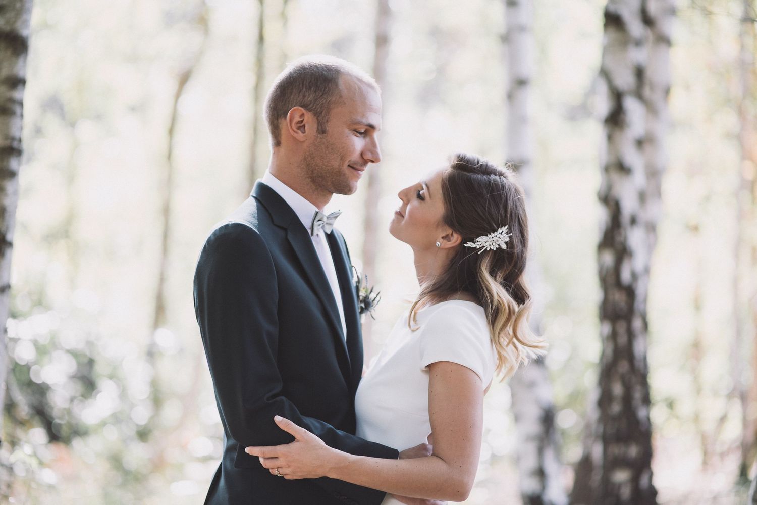 A bride and groom share an intimate moment while dancing together in a sunlit birch tree forest.