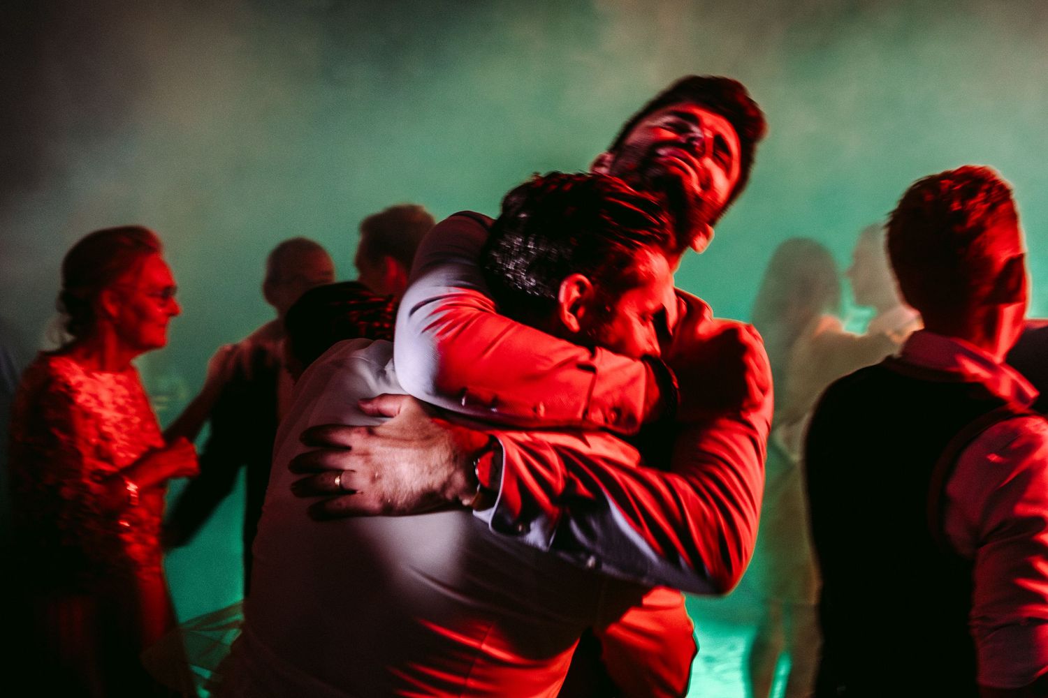 Two people embrace in an intimate hug on a dance floor with red lighting and fog in the background.