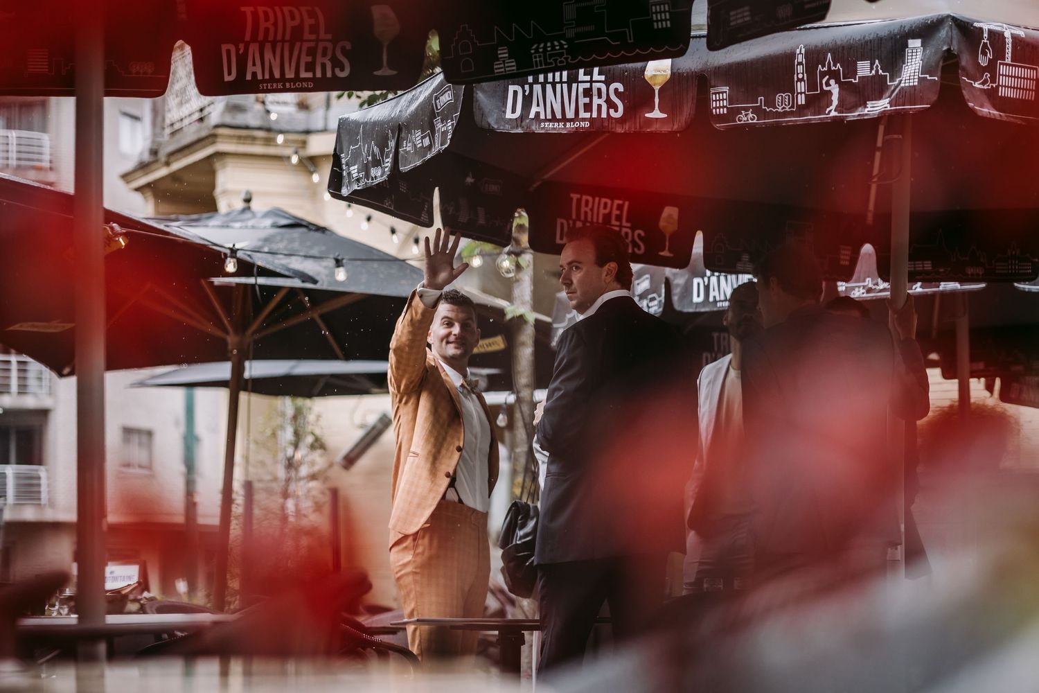 Blurred red flowers frame an urban street scene with outdoor restaurant seating and historic buildings.