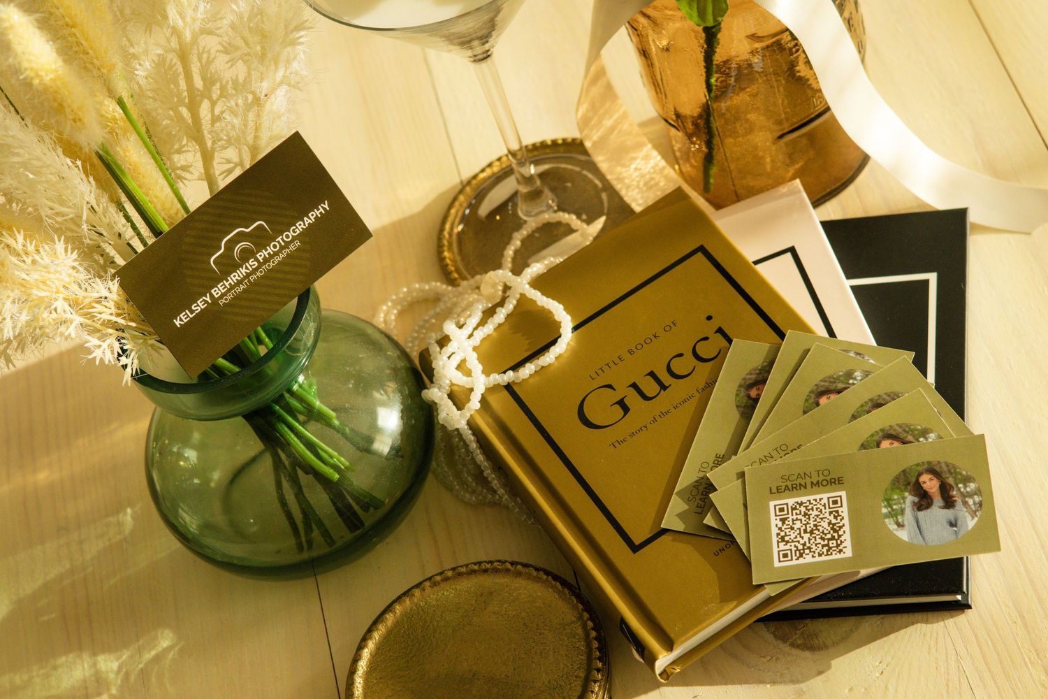 Gucci book, green glass vase with dried flowers, business cards, and decorative items on a light surface.