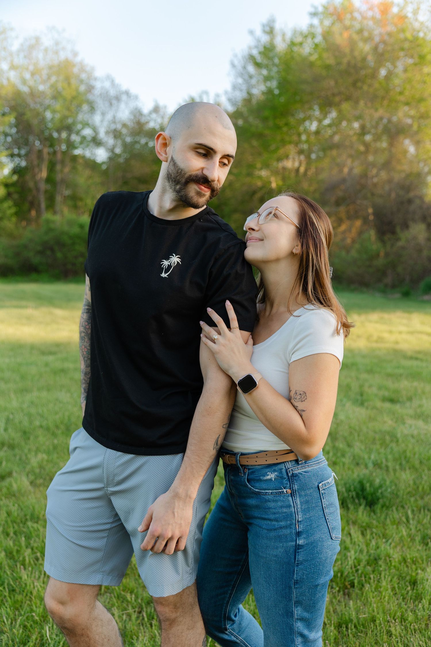 Smiling couple standing together in green park, tattooed bald man in black shirt with woman in white top.