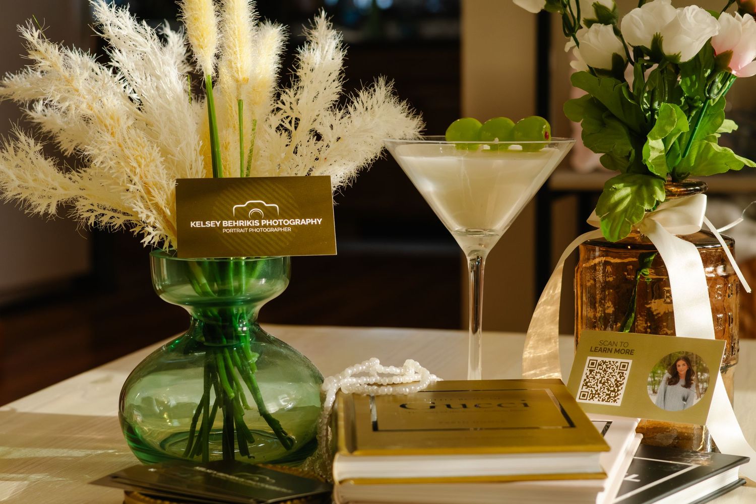 Elegant table display with green vase, pampas grass, martini glass, and gold business cards for a photographer.